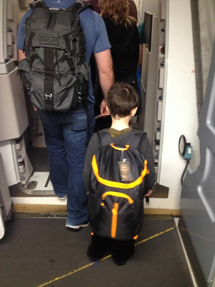 Getting on the plane. His backpack is bigger than he is. 